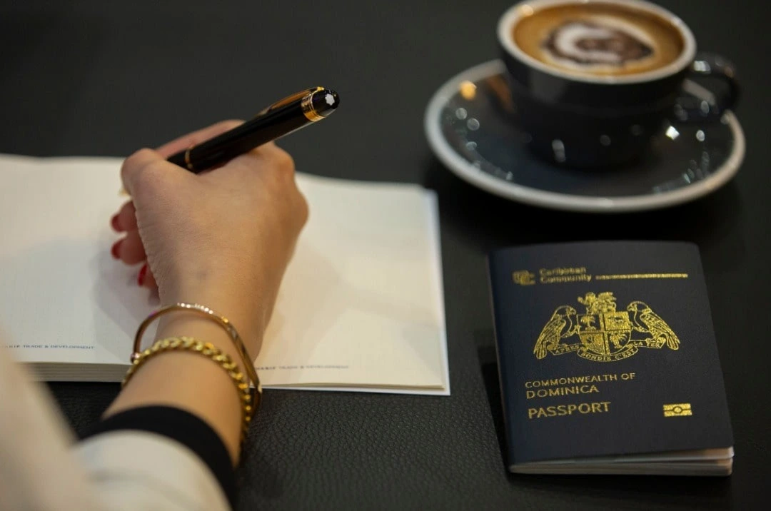 woman writing while there is dominica passport and coffee on table - shariftrip; get passport and citizenship of best country